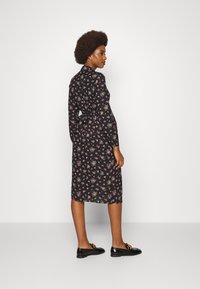 Vestido preto com flores, mangas longas, cintura ajustada e comprimento até o joelho. Apresenta pequenas flores rosa e verdes e uma textura de tecido suave. Sapatos loafers pretos.