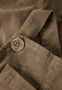 Brun kordfløjl med en tekstureret overflade, der har en stor træknap og justerbar rem. Synlig syning og lomme detaljer.