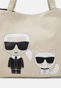 Torba płócienna z beżowym tłem, na którym narysowany jest mężczyzna w czarnym garniturze i kot, obaj w okularach przeciwsłonecznych, ilustrowani w czerni i bieli.