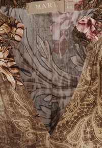 Brunt mønstret stof med blomster- og paisleymønstre; har en v-udskæring og rynkede detaljer ved ærmekanterne. Mærkelabel synlig.