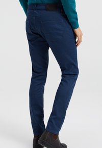 Navy blue, slim-fit pants with a smooth texture, five pockets, and a stitched logo patch on the waistband.