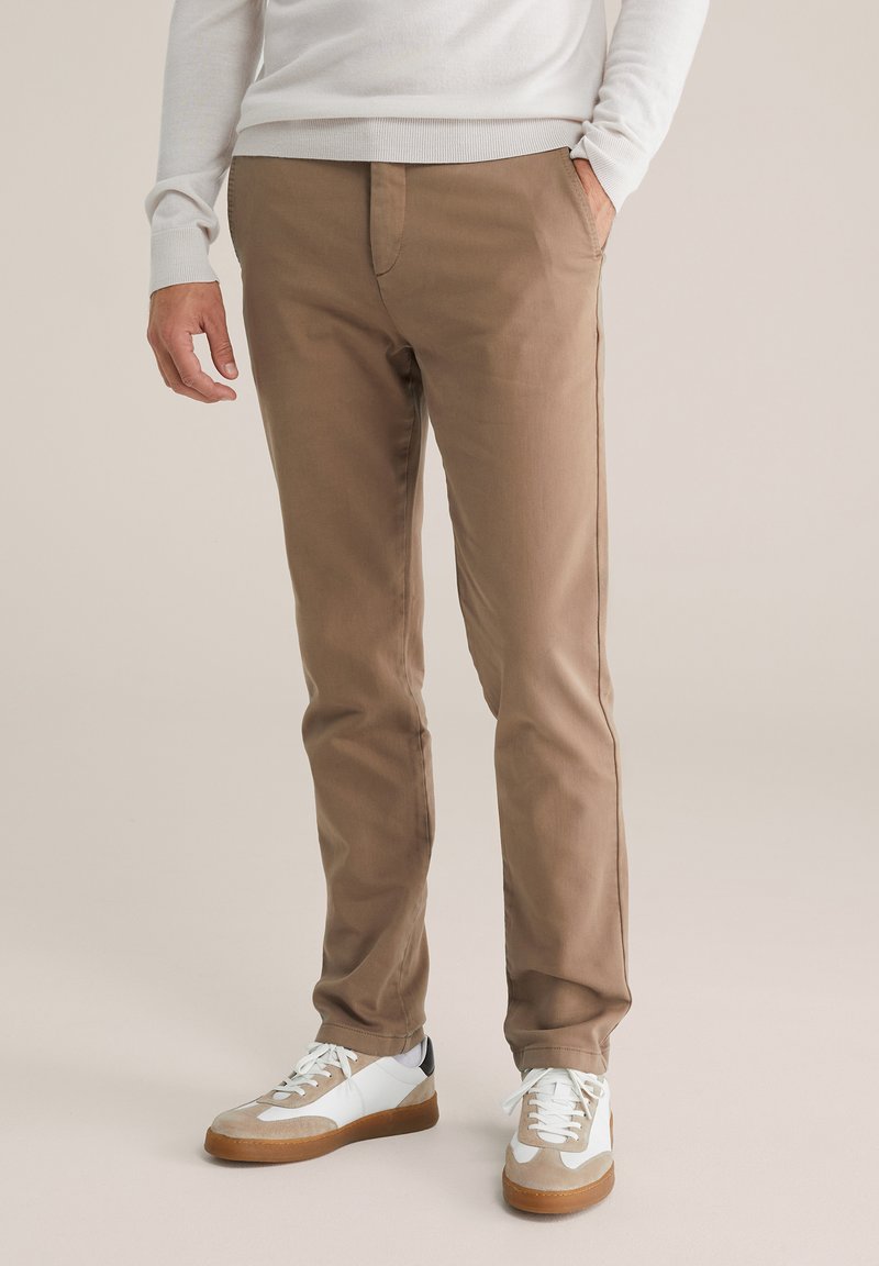 Beige bavlněné kalhoty slim fit s předními kapsami, doplněné bílými a šedými teniskami s hnědou gumovou podrážkou.