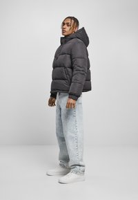 Schwarze Daunenjacke mit Kapuze und horizontalen Steppnähten. Kombiniert mit hellblauen, locker sitzenden Jeans und weißen Sneakers.