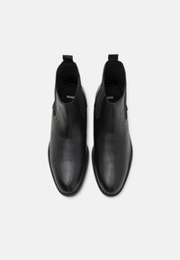 Bottes chevilles en cuir noir à finition lisse, avec des panneaux latéraux élastiques et une languette à l'arrière. Semelle intérieure matelassée pour le confort.