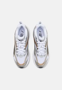 Zapatillas deportivas blancas con acentos en plata y oro, tejido de malla, puntera redonda y suela plana. Diseño con cordones y detalle de tirador en la parte trasera.
