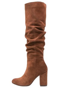 Bottes en suède marron, montantes jusqu'au genou, au design décontracté, avec un bout arrondi et un talon épais, présentant des plis subtils pour une texture ajoutée.