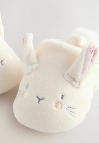 Chaussons en polaire ivoire douce avec un visage de lapin brodé, de longues oreilles et des détails roses. Forme arrondie avec une texture moelleuse.
