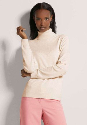 Lichtbeige coltrui van gebreid materiaal met geribde manchetten en zoom, gecombineerd met roze broek. Soepele textuur, relaxte pasvorm.