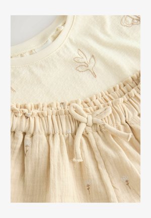 Bombažna obleka z vezenimi cvetličnimi vzorci v bež barvi. Ima zbrano pasnico z nastavljivim trakom in mehko, teksturirano tkanino.