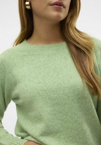 Maglione verde chiaro in tessuto morbido e testurizzato, con scollo a girocollo e maniche raglan. Caratterizzato dalla sua apparenza melangiata.