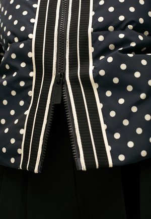 Navy blue polka dot puffer jacket featuring a contrasting white zipper and striped trim along the front. Smooth texture, short sleeves.