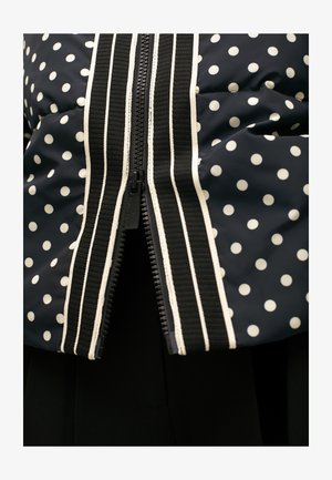 Marineblauer Puffer-Jacke mit Polka-Dots, ausgestattet mit einem kontrastierenden weißen Reißverschluss und gestreiftem Besatz an der Vorderseite. Glatte Textur, kurze Ärmel.