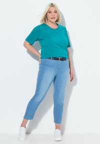 Tyrkysové tričko s krátkým rukávem v kombinaci se světle modrými slim-fit džíny a bílými teniskami, doplněné námořnickým páskem a jemnou, hladkou texturou.