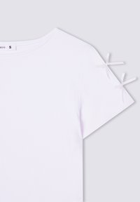 T-shirt bianco a costine con maniche corte, caratterizzato da piccoli fiocchi bianchi sulle cuciture delle spalle. Il tessuto appare morbido e leggero.