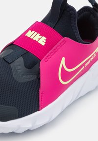 Czarno-różowe trampki z teksturowaną siateczkową cholewką, wyrazistym żółtym logo Nike, elastycznym paskiem oraz białą podeszwą z wzorem bieżnika.