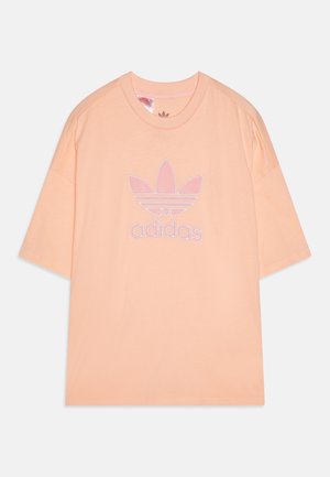 Koszulka z krótkim rękawem w kolorze brzoskwiniowym z okrągłym dekoltem, z dużym różowym logo Adidas trefoil i napisem „adidas” z przodu.