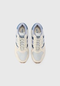 White and light blue sneakers with mesh and suede materials. Features three blue stripes, round toe, padded collar, and rubber sole.
