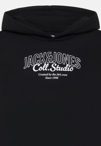 Hoodie noir en matériau doux, avec un grand logo texte graphique blanc portant "JACK&JONES Coll. Studio" à l'avant.