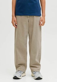 Pantalones de pierna ancha beige hechos de algodón suave, con un patrón liso y un ajuste relajado. Combinados con zapatillas deportivas grises y blancas.