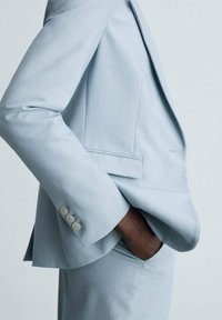 Jasnoniebieska marynarka z teksturowanej tkaniny, z pojedynczą kieszenią na piersi i detalami na mankietach w postaci dwóch guzików, o dopasowanym fasonie.
