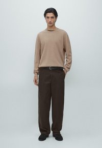 Beige stickad tröja med långa ärmar, matchad med mörkbruna vida byxor och svarta skor. Enkel design med avslappnad passform.