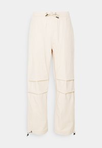 Beige Cargohose mit elastischem Bund, Zugbandverschluss, Seitentaschen und verstellbaren Beinenden; hergestellt aus leichtem Stoff mit glatter Textur.