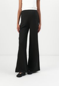 Svarte vide bukser med stretchliv, laget av myk, flytende stoff. Kombinert med svarte perle-dekorerte slip-on sko.