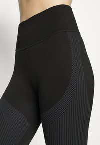 Zwarte leggings met een brede geribbelde tailleband, voorzien van textuurpanelen met strepen en stippenpatronen langs de zijkanten. GLadde stofafwerking.