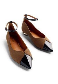 Ballerines en daim marron avec un bout pointu en cuir verni noir. Présentent une sangle à la cheville et un intérieur lisse. Design minimaliste avec un accent métallique.