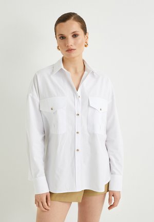 Camisa blanca de botones con cuello, dos bolsillos en el pecho, botones en tono dorado y mangas largas; fabricada en un tejido ligero.