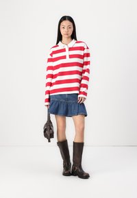 Haut à manches longues rouge et blanc rayé avec un col, associé à une jupe en denim avec un ourlet volé, et des bottes en cuir marron jusqu'aux genoux.