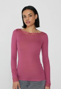 Langärmliges, enganliegendes Oberteil in Mauve mit gewelltem Spitzenbesatz am Ausschnitt und an den Bündchen, aus weichem, dehnbarem Material.