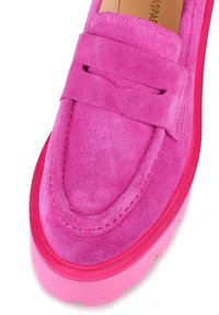 Klarröd mocka loafers med tjock sula och bred rem över toppen, som visar detaljerad sömnad och textur.