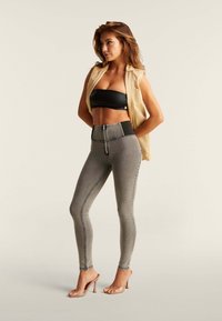 Korkeavyötäröiset harmaat skinny farkut, joissa on kontrastiväriset tikkausviivat ja etuvetoketju. Yhdistetty mustan bandeautopin ja hihattoman beigebalin takin kanssa.