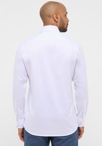 Camicia bianca a maniche lunghe con sottili strisce blu, colletto classico, polsini con bottone e orlo curvato. Realizzata in morbido tessuto di cotone.
