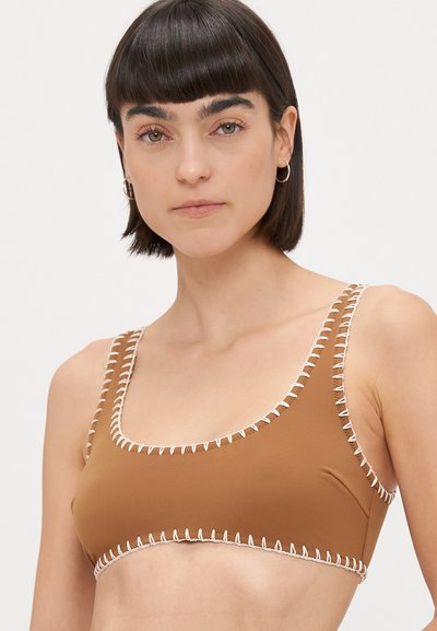 Smeđi bikini top od glatkoga materijala, s bijelim šavovima duž rubova. Imajte izrez u obliku žlice i široke naramenice za podršku.