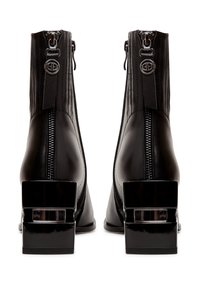 Bottes cheville en cuir noir avec fermetures éclair à l'arrière, tirettes décoratives en métal avec logo, et talons blocs épais avec détails de découpe rectangulaire.