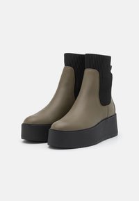 Greige faux leather ankle boots with a ribbed black textile upper, thick black platform sole, and elastic side panels for easy wear.