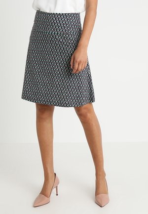 Et knælængde skørt lavet af stof med et geometrisk mønster i marineblå, grøn og hvid. Kombineret med lyserøde spidse hæle.