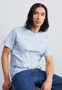 Lyseblå bomulds t-shirt med rund hals, korte ærmer og et lille blåt Jumpman-logo på brystet. Båret sammen med blå denimjeans.