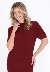 Burgundy ribbattu knit sweater, jossa on tiukasti istuva siluetti, lyhyet hihat ja korkea kaulus. Teksturoitu kangas, jossa on sileä pinta.