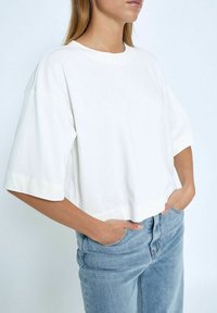 Camiseta blanca de algodón recortada, con mangas cortas, escote redondo y un corte relajado. Combinada con jeans de denim azul claro.