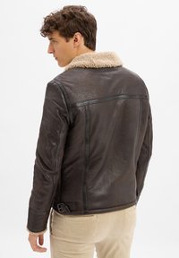 Brązowa skórzana kurtka z odpinanym beżowym kołnierzem z owczej wełny, gładka faktura, dopasowany krój i zapięcie na klamrę w pasie.