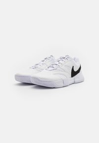 Hvite treningssko med mesh- og syntetisk overdel, med en svart swoosh-logo, teksturert såle og snøring foran.