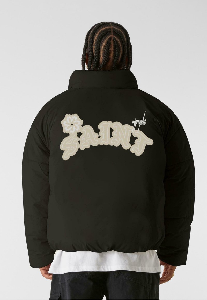 Giubbotto imbottito nero con vestibilità oversize, caratterizzato da testo "SAINT" color crema e design floreale sul retro, e colletto alto.