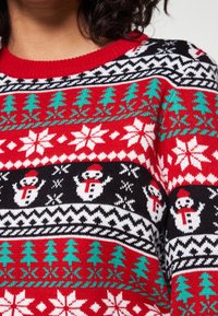 Roter Pullover mit Feiertagsmustern, die Schneemänner, Schneeflocken und Bäume in Weiß, Schwarz und grünem Strick zeigen. Klassischer Rundhalsausschnitt.