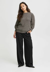 Sweater en tricot gris foncé avec un motif en câble texturé, associé à un pantalon large noir taille haute et des chaussures noires à bout pointu.
