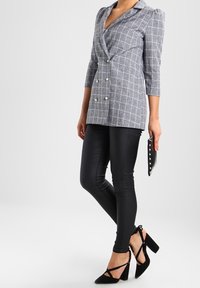 Grå rutig kavaj med trekvartslånga ärmar, dubbelknäppt design och pärlknappar. I kombination med svarta leggings och sandaletter.