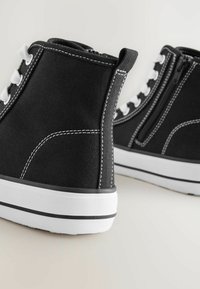 Zwarte canvas hoge sneakers met witte stiksels, oogjes en veters; voorzien van een zijrits en een witte rubberen zool met zwarte accenten.