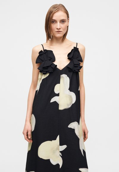 Μαύρο φόρεμα με μεγάλο λευκό ανθικό σχέδιο, με βολάν στους ιμάντες των ώμων και ντεκολτέ σε σχήμα V. Ελαφρύ ύφασμα.